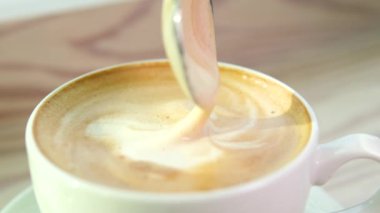 Kahveyi bardakta kepçeleyen bir kaşığı tutan bir el. Lezzetli kremalı bir fincan Cappuccino kahvesi. Yüksek kalite 4k görüntü