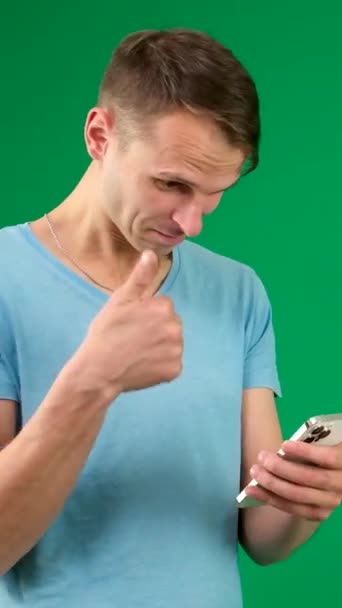 若いプロモーターの男はシャツの白いTシャツのポイント指の指のカメラを身に着けますワークスペース区域のコピースペースのモックアップを指示します 明白なパステル ライト グリーンの背景 — ストック動画
