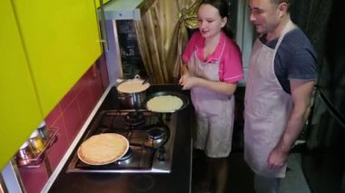 Krepleri evde kızartma tavasında pişir, hamuru kızartma tavasına dök, çevir, çevir, çevir, incele, büyük krep, kırmızı fayans, mutfak. Babası olan genç bir kız ince krepleri tavada çevirmeyi öğreniyor.