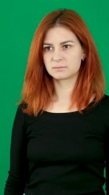 dikey video. Alıngan dudaklar öne çıkar. Gözleri yuvarla. Yeşil renkli arka plandaki genç, kızıl saçlı bir kadının negatif duyguları. Kanada. 