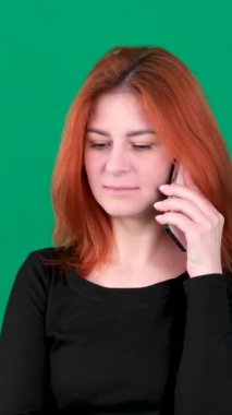 Genç kızıl saçlı kadın evde ciddi bir ifadeyle akıllı telefondan konuşuyor. Yüksek kaliteli FullHD görüntüler