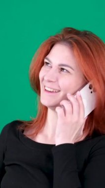  dikey video. Krom anahtar stüdyo duygularında yeşil arka planda olan kızıl saçlı genç bir kadın. Kahverengi gözlü, açık tenli, Avrupalı Amerikalı. Kanadalı. Telefon, İş kadını telefonda konuşuyor., 