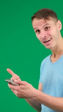 Elinde akıllı telefon olan hoşnutsuz genç bir adam mavi bir arka planda duruyor, boş bir alanda parmağını yana doğrultuyor ve kameraya sarkastik bir yüzle bakıyor. Yüksek kalite 