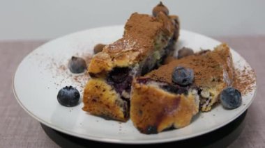 Tahta masadaki beyaz seramik tabakta ev yapımı taze pişmiş yaban mersinli cheesecake dilimini alıyorum. Böğürtlen ve tarçınlı kek.