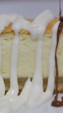 Cheesecake diliminin üzerine çikolata sosu dökülüyor. Çikolata soslu vejetaryen hindistancevizli kaju peynirli kek dilimi. Yüksek kalite 4k görüntü