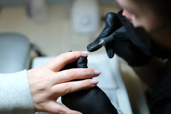 Close up shot of woman in nail salon receiving manicure by beautician with metal nail file. Woman getting nail manicure at spa centre. Beautician file nails to a customer in luxury salon. High quality