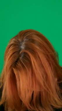 dikey video. Krom anahtar bir stüdyoda, yeşil arka planda, kırmızı saçlı genç bir kadın. Yakın çekim, kahverengi gözler. Üzüntü, melankolik saçlar, genç bir kadının koyu renk gözleri. kızıl saçlı. 