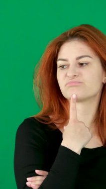 dikey video. Krom anahtarlı stüdyo duygularında yeşil arka planda olan kızıl saçlı genç bir kadın dudaklarını öne çıkararak parmaklarını hoş olmayan duygulara bastırdığını düşünür. Dişlerini sık.
