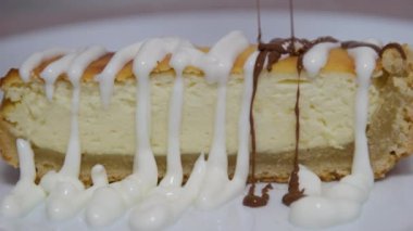 Cheesecake diliminin üzerine çikolata sosu dökülüyor. Çikolata soslu vejetaryen hindistancevizli kaju peynirli kek dilimi. Yüksek kalite 4k görüntü