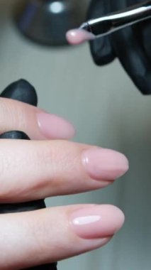 Tırnak manikürünün ayrıntıları dosya ya da fırçayla. Güzel bir tırnak bakımı. Siyah eldivenli manikürcü bej rengi nötr renkte jöle cilasıyla yakın plan güzellik salonu manikürcüsü.