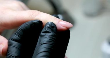 Tırnak manikürünün ayrıntıları dosya ya da fırçayla. Güzel bir tırnak bakımı. Siyah eldivenli manikürcü bej rengi nötr renkte jöle cilasıyla yakın plan güzellik salonu manikürcüsü.