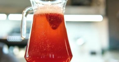 Açık büfe masasına yakın çekim, beyaz masa örtüsü ile ahşap masa örtüsü üzerinde soğuk taze komposto içeceği ve boş bardaklarla dolu cam sürahiler var. Görünür insan siluetleri. Yüksek kalite