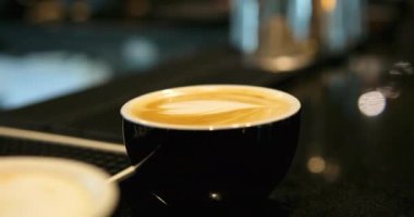Küçük siyah minimalist kahve fincanlarına kapuçino ve sıcak süt köpüklü latte sanatını yavaş çekimde yakından izle. Siyah bardakta yüksek kaliteli kahve.