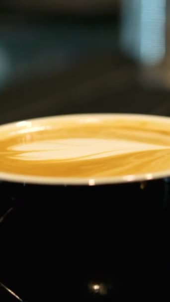 用卡布奇诺咖啡和热牛奶泡沫拿铁艺术慢动作的小黑色简约咖啡杯的近景 高质量的黑杯子咖啡 — 图库视频影像