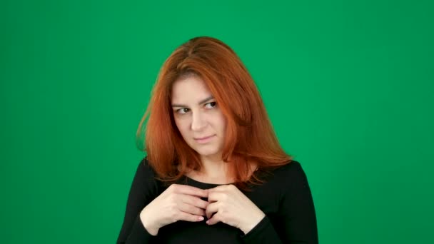 红头发的年轻女性 背景是绿色的 在一个彩色的关键工作室里 她的情绪期待着一次经验 把你的手指交叉在胸前 这让你的眼睛对一次经历感到尴尬 不确定性 — 图库视频影像