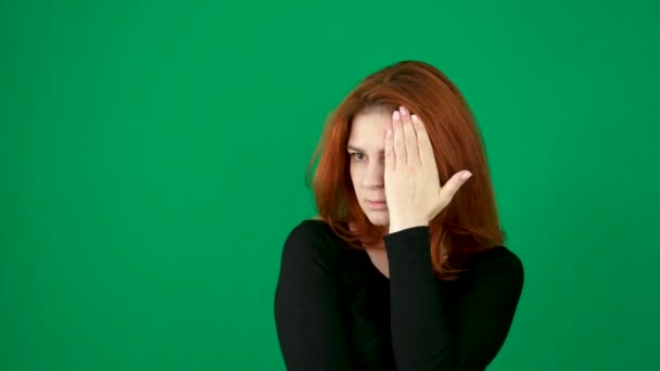 红头发的年轻女人在绿色的背景上用你的手 视力测试 一只眼睛看着绿色的背景 穿着黑色夹克的红头发女人 — 图库视频影像