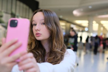 Mutlu, gülümseyen, uzun saçlı liseli bir kızın portresi boş bir sınıfta kameraya bakarak selfie çekiyor. Yüksek kalite fotoğraf