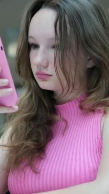 Kız arkadaşlarıyla telefonda konuşuyor ve alışveriş merkezindeki bir restoranın arka planına karşı çıkıyor. Pembe telefon kılıfı gülümse beyaz ten, Avrupa, Amerikan iletişim alışveriş interneti