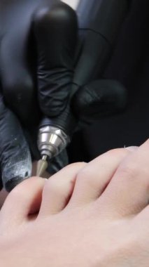 Kuaför salonundaki pedikür uzmanı, güzellik salonundaki ayak temizleme videosuyla ilgileniyor. Tırnaklarını törpülüyor. Siyah eldiven reklamında masaj yapıyor. Bir kadın videosunun hayatı.