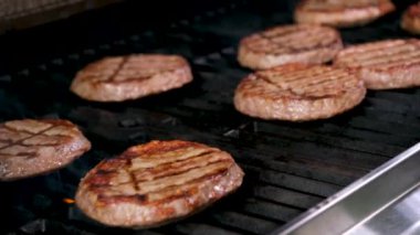 Şef barbekü sahnesi hamburgerleri pişirirken ızgarada bir spatula çevirici ve sakin bir ateş alevi vardı. Yüksek kalite 4k görüntü