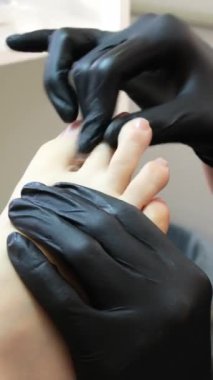 Kuaför salonundaki pedikür uzmanı, güzellik salonundaki ayak temizleme videosuyla ilgileniyor. Tırnaklarını törpülüyor. Siyah eldiven reklamında masaj yapıyor. Bir kadın videosunun hayatı.