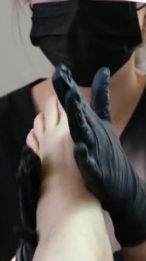 Kuaför salonundaki pedikür uzmanı, güzellik salonundaki ayak temizleme videosuyla ilgileniyor. Tırnaklarını törpülüyor. Siyah eldiven reklamında masaj yapıyor. Bir kadın videosunun hayatı.