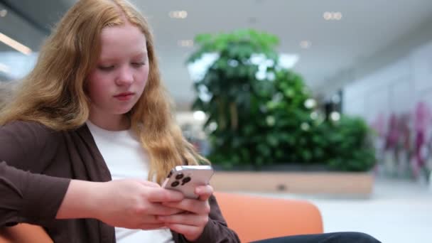商场里的一个女孩坐在电话里与朋友们交流 在网上购物 接听无线网络游戏 看新闻 高质量的 — 图库视频影像