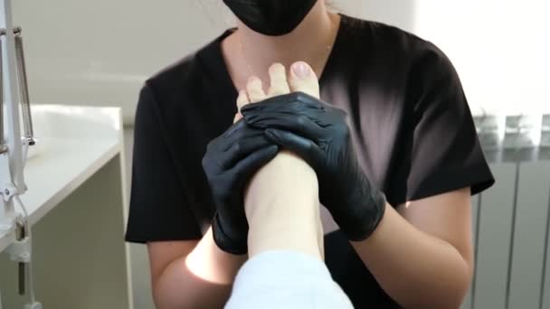 专业的足底按摩在修脚沙龙护理女医生的黑色手套和面具做按摩与圆形膝关节运动足部治疗问题的恢复 修脚沙龙 — 图库视频影像
