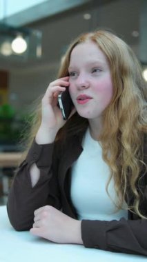 Telefonda konuşan kızıl saçlı kız açık tenli çiller alışveriş merkezindeki kafede oturmuş arkadaşlarıyla iletişim kuruyor kırmızı yanaklar utançtan kızarıyor bir erkekle ilk aşk sohbeti. İlk randevu daveti