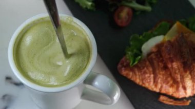 Taze kruvasan ile servis edilen bir fincan kibrit çayı latte. Elin bardağı alıyor. Yüksek kalite 4k görüntü