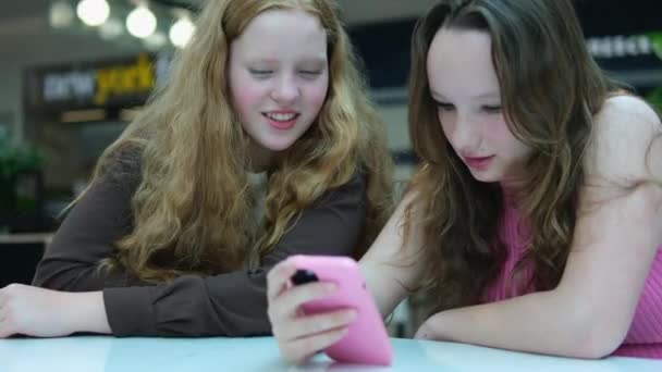 モバイルゲームをしているスマートフォンを見ている2人の若い女の子の近くで ソーシャルメディアでチャット 高品質の4K映像 — ストック動画