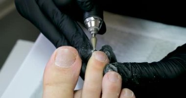 Kuaför salonundaki pedikür uzmanı, güzellik salonundaki ayak temizleme videosuyla ilgileniyor. Tırnaklarını törpülüyor. Siyah eldiven reklamında masaj yapıyor. Bir kadın videosunun hayatı.