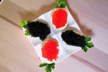 Ahşap zemin üzerinde kırmızı havyar olan haşlanmış tavuk yumurtasının yarısı. Yumurtanın üzerine siyah havyar koyun. Lezzetli ve sağlıklı yemekler servis etmek için.