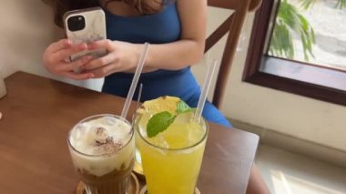 Masada üç farklı içecek. Sağlıklı yiyecek suyu. Ananas suyu. Tuzlu karamel Latte ve buzlu yeşil çay. Spor salonundaki kız kafeteryada cep telefonuyla dinleniyor..