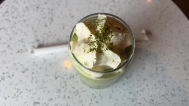 Matcha latte hazırlamak süt ve buz küplü, süt köpüğünün üzerine yeşil toz kibrit serpmek, yüksek kaliteli dikey video klipsi, bir bardak yeşil buzlu çaya süt dökmek, 