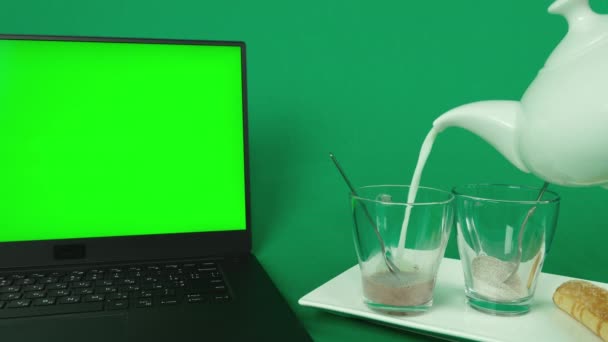 黑色笔记本电脑 鼠标绿色背景 白盘上有两个杯子 里面有咖啡和可可 还有两个新鲜面包 把热牛奶倒进杯子里 — 图库视频影像
