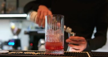 Barmen bir parça portakal kabuğunu sıkıyor ve bardaki negroni kokteylini süslüyor. Yüksek kalite 4k görüntü