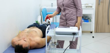 Hemşire erkek hastayı EKG testine hazırlıyor. Klinik hastanesi sağlığı izliyor