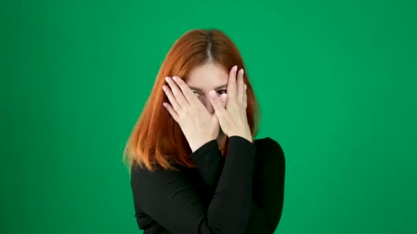 一个黑衣女孩 红头发 双手捂住眼睛 用手指看过去 绿色背景 年轻女人的情绪近视棕色眼睛浅色皮肤的美籍欧洲人 加拿大 — 图库视频影像