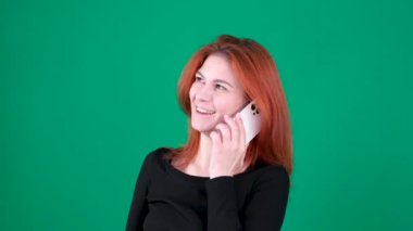 Kızıl saçlı kız telefonda konuşuyor, gülümsüyor, tatmin olmuş, mutlu. Yeşil arka plan. El hareketi kızıl saçlı kadın. Krom anahtar duygular. Kapalı kahverengi gözler. Kanada