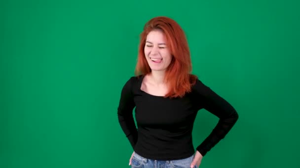 一个红头发的女孩面带微笑 在绿色的背景上表现出不同的情绪 穿着黑色衣服和蓝色牛仔裤的白人女孩 高质量的4K镜头 — 图库视频影像