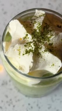 Matcha latte hazırlamak süt ve buz küplü, süt köpüğünün üzerine yeşil toz kibrit serpmek, yüksek kaliteli dikey video klipsi, bir bardak yeşil buzlu çaya süt dökmek, 
