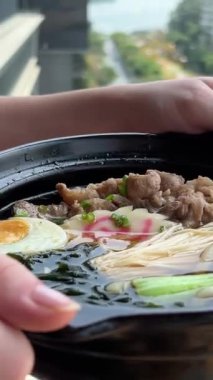 Asya erişte çorbası, tavuklu ramen, tofu, sebze ve siyah kasede yumurta. Geçmişi sil. Üst Manzara. Yüksek kalite Bir kız elinde sıcak çorba taşır