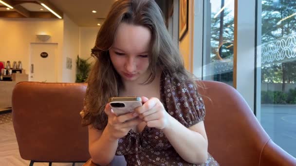 トウモロコシフラワーブルーセーターのティーンエイジャーの学生は スマートフォンやチャットをテキストを使用して 女性の手は 携帯電話を保持し 自宅の朝にリビングルームでモバイル上のメッセージを入力します 閉じる ビュー — ストック動画