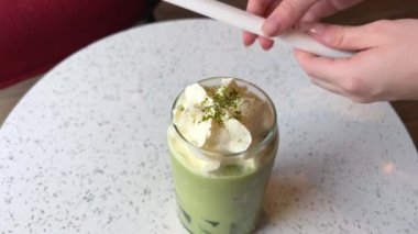 Mükemmel bir bardak sağlıklı yaz içeceği, genç bayan bardağa bir pipet yerleştiriyor ve kibrit yeşil çay ile sütü eşit ve içmeye hazır hale getiriyor. Yüksek kalite 4k görüntü