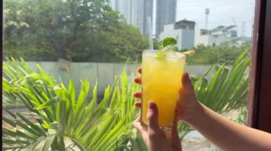 Ananas suyu, kadın kız tomarlarının ellerinde ve Vietnam 'daki bir pencerenin arka planına samanla servis edilen uzun süredir bardakta duran nane şekerli meyveye bakıyor. Sağlıklı suyu karıştıran kadın elinin yakın çekimi