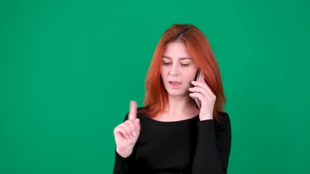 女の子は電話で と言い 手をノーと言い 緑色の背景に黒い服を着ました 赤い髪の若い女性クロマキースタジオ感情ライトスキンヨーロッパのアメリカ人 カナダ — ストック動画