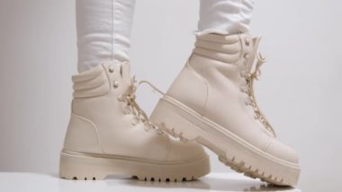 Dişi, traktör tabanındaki beyaz botları çeker ve dili tutar. Modern sonbahar ayakkabılarını gösteren bir model. Yüksek kalite 4k görüntü