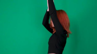  Siyah elbiseli kız ellerini kaldırıp ellerini indiriyor, saçlarını okşuyor. Yüksek kalite 4K görüntüler, kızıl saçlı genç bir kadın yeşil arka planda, yakın plan stüdyo duygularında. 