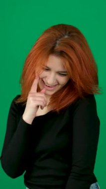Kızıl saçlı kız, gülümsüyordu, parmağını sağ yanağına kaldırdı, başını eğdi ve utangaç oldu. Krom anahtar stüdyo duygularında yeşil arka planda genç bir kadın. Kahverengi gözler. Açık ten. 